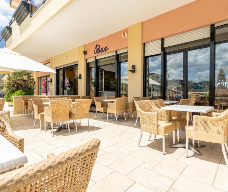 Terrazza di un bar con sedie in vimini e tavoli all'aperto.